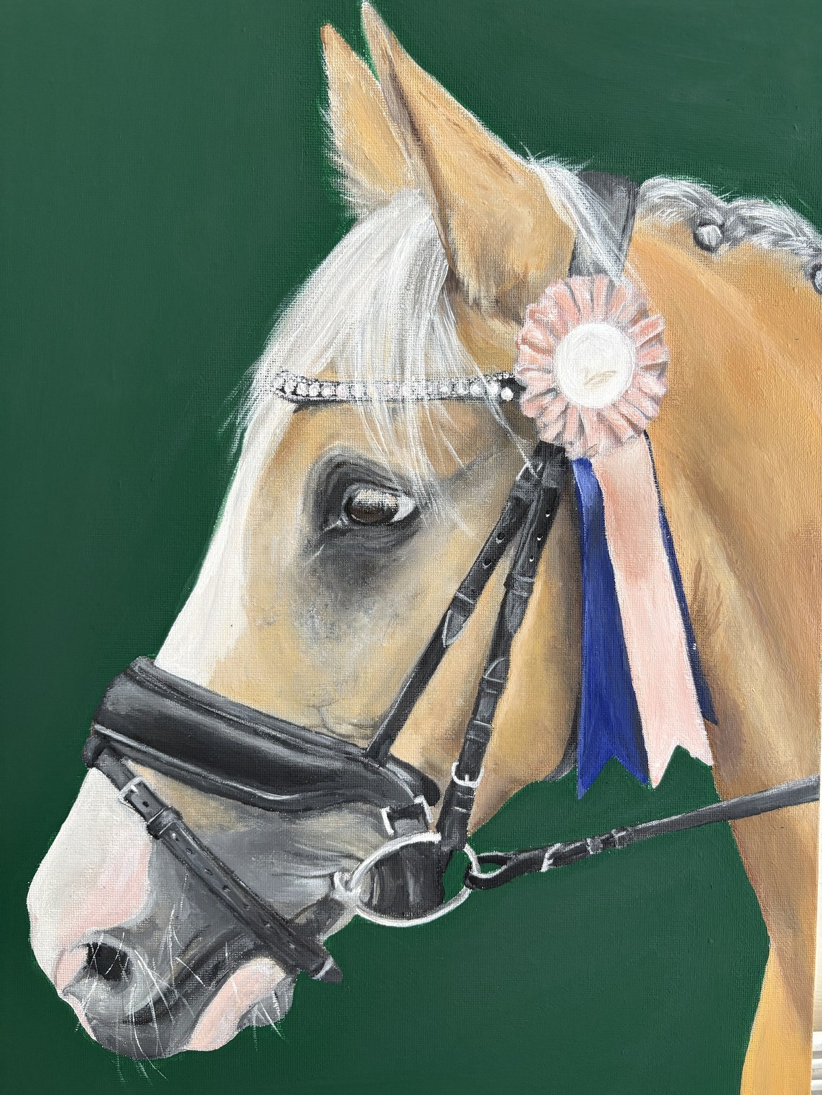 Close portrait of a palomino pony's head in full show tack, wearing a diamante browband and a pink rosette, against a dark green background.